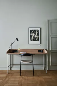 A minimalist home office featuring a wooden desk with metal legs, a black table lamp, and a black and white abstract artwork 