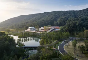 A serene landscape featuring concrete structures amidst lush greenery and a serene pond, surrounded by rolling hills.