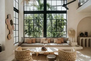 A modern, minimalist living room with a large window, concrete walls, and wicker chairs.