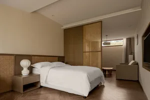 A minimalist bedroom featuring a modern white bed with wooden furnishings and a central wooden partition wall.