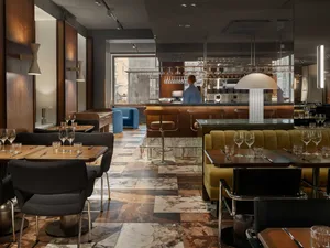 Modern restaurant bar with marble countertops, leather seating, and wooden tables and chairs.