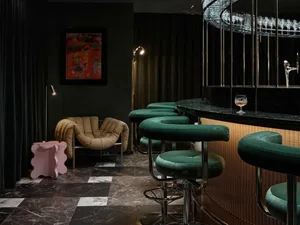 Modern restaurant bar area featuring velvet stools, marble flooring, and metal bar counter.