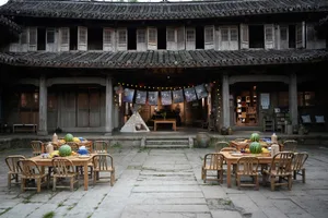 Outdoor seating area with wooden tables and chairs in front of a traditional Chinese building with a tiled roof and wooden sh