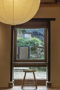 Traditional interior view featuring a window showing a view of a rustic, stone-walled garden with wooden elements.