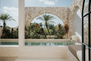 A vintage stone backyard featuring a pool surrounded by lush plants and a stone archway.