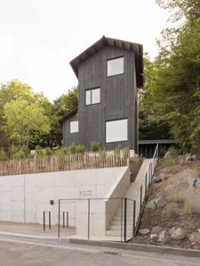 A modern house with a black wooden exterior, featuring a steep roof and large windows.