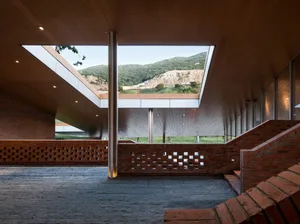 A modern architectural interior featuring brick walls, concrete details, and large windows overlooking a natural landscape.
