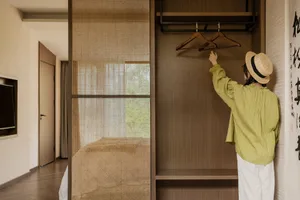 A person wearing a straw hat interacting with an empty wooden wardrobe.