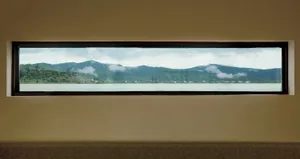A rectangular window overlooking a serene lake surrounded by mountains and clouds in the background.