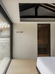 A minimalist bedroom with wooden flooring, a bed, and a simple white wall with a wooden door.