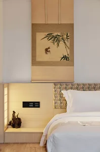 A minimalist bedroom with a wooden headboard, white bedding, and a framed painting above the bed.