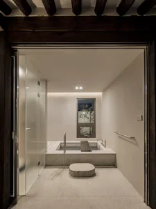 Modern bathroom featuring a concrete and glass interior design, with a square bathtub surrounded by minimalist elements.