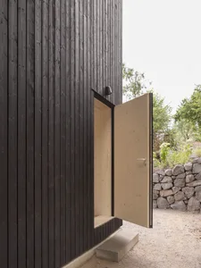 Modern exterior of a building with dark, horizontal wood planks and an open wooden door.