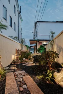 A modern garden pathway made of natural stone leads through a lush green garden with various plants and trees.