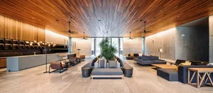 A spacious, modern industrial hotel lobby featuring concrete walls, a high wooden ceiling, comfortable seating areas, and a c