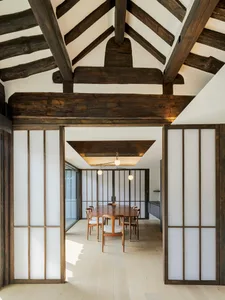 A modern dining room with wooden beams on the ceiling, featuring a wooden table and chairs.