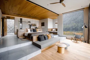 A modern minimalist bedroom with a large window overlooking a natural landscape, featuring a bed with black and white pillows
