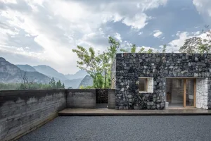 現代住宅石造房屋，外牆採用石材，搭配大型窗戶，眺望山巒與樹木。