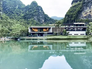 Modern resort with concrete and glass structure surrounded by greenery and water.