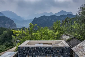 一座石牆住宅，背靠茂密綠意山巒與繁盛植被。