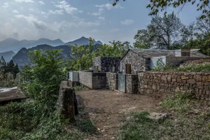 A rural house made of stone surrounded by trees and mountains