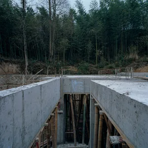 Concrete construction foundations with bamboo scaffolding in a forested area.