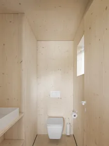 A minimalist bathroom with wooden paneling, featuring a white toilet and sink.