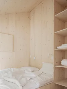 A minimalist bedroom with white wood walls and a bed with white bedding.