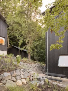 Modern minimalist building with black exterior, stone walls, and metal accents surrounded by greenery.