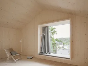 A minimalist window seat made of wood with a cushion and a gray curtain.