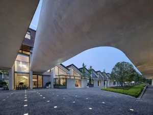 A modern architectural structure made of concrete with a curved concrete overhang and a courtyard area.