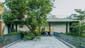 A modern building with a concrete facade and glass elements surrounded by green trees and mountains.