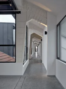 A modern corridor featuring white concrete walls, glass windows, and a polished floor, with arches and industrial lighting.