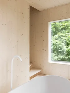 Modern minimalist bathroom featuring wood-paneled walls, a white bathtub, and a set of stairs.