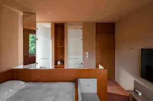 A modern minimalist bedroom featuring a bed, two chairs, and a television in a minimalist design with wooden and textile elem