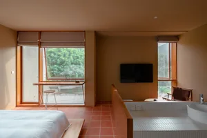 A modern residential room with tiled floor, large windows showing greenery, and a bathtub with a view.