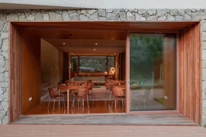 Modern restaurant interior with wooden tables and glass windows overlooking green landscape.