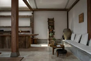 A minimalist living room with concrete walls, wooden furniture, and a simple design.