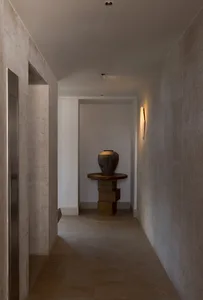 極簡風格的走廊，混凝土牆面與地板，木質基座上擺放大型花瓶。