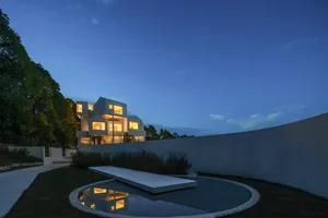 A modern, minimalist residential exterior with a courtyard and pond at dusk.