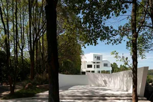 A modern haunted house with a white concrete exterior surrounded by trees and a white pathway.