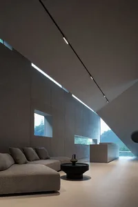 Modern living room with concrete and glass walls, featuring a contemporary sofa and minimalist decor.