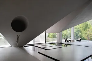 Modern living room with concrete floor, walls, and ceiling, featuring large windows and minimalist furniture.