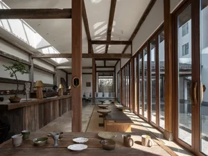 A spacious, modern restaurant interior featuring a wooden counter, chairs, and various tableware items on a counter.