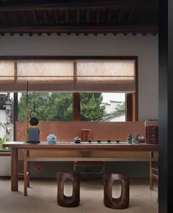A traditional tea room with wooden furniture and decorative elements, featuring a tea table, stools, and a window view of gre