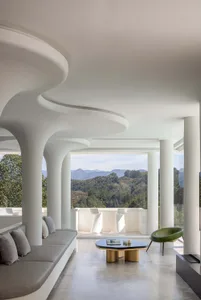 A modern living room with a concrete ceiling and floor, featuring a curved sofa, a round black coffee table, and a view of th
