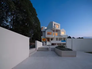 A minimalist, modern white house with a concrete exterior at dusk.