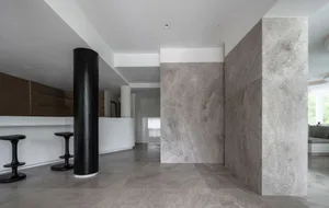 A modern minimalist lobby with concrete walls and floor, featuring sleek black stools and a white reception desk.