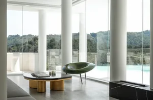 Modern minimalist living room featuring glass walls, concrete floor, and green seating area.