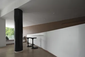 Minimalist interior with concrete barstools and a large black column.